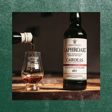 A photo of a Laphroaig bottle next to a dram being filled on green paper background