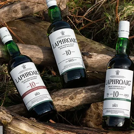 Three bottles of Laphroaig lying on tree trunks