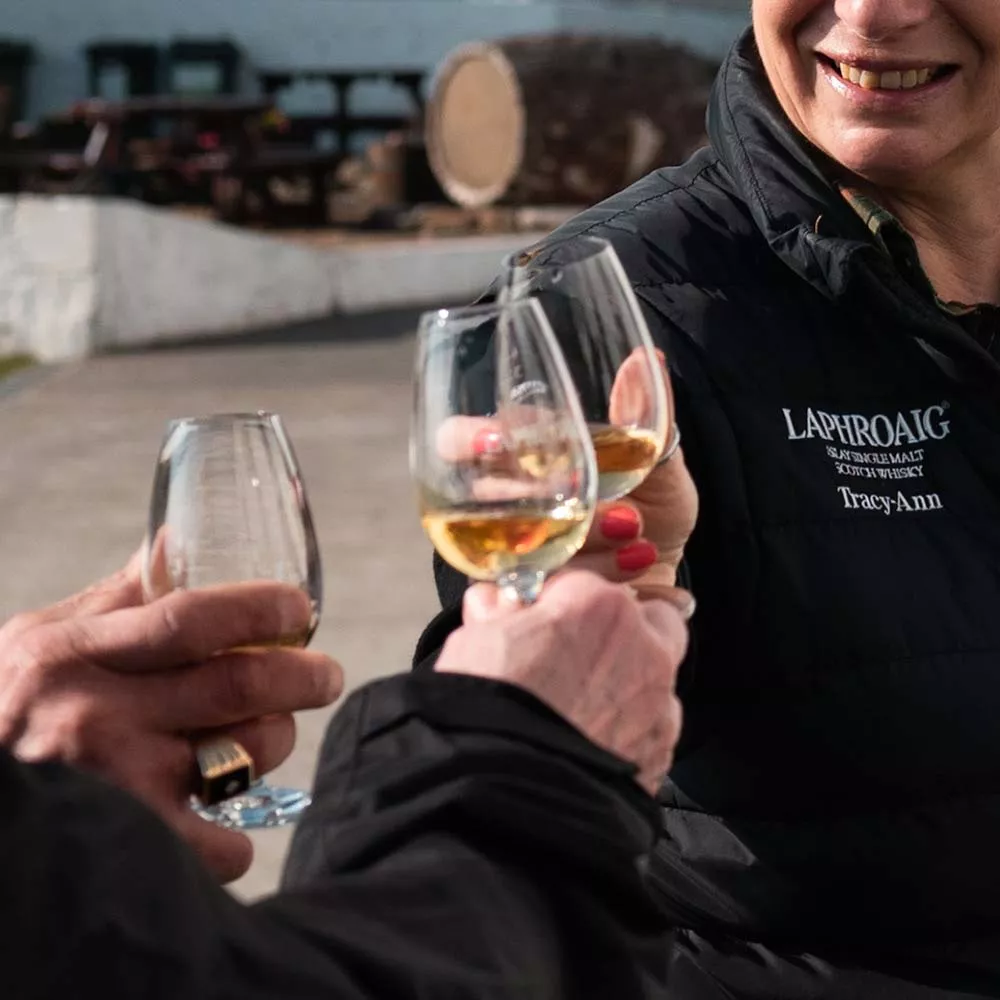 Three people toasting glasses of Laphroaig whisky outdoors