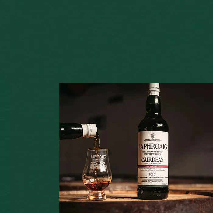 A picture of a Cairdeas Laphroaig bottle with a dram being filled beside it, on dark green background