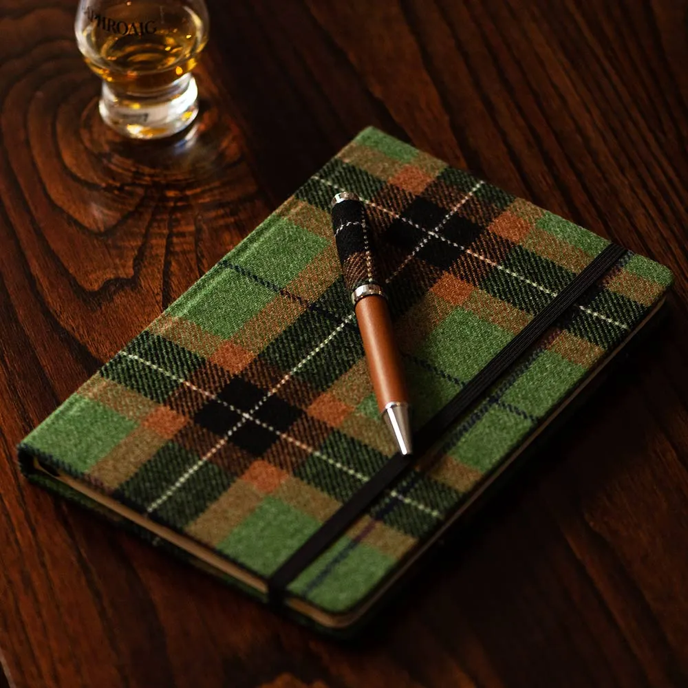 Checkered whisky tasting notebook on a wooden table with a pen on top and a filled dram beside it