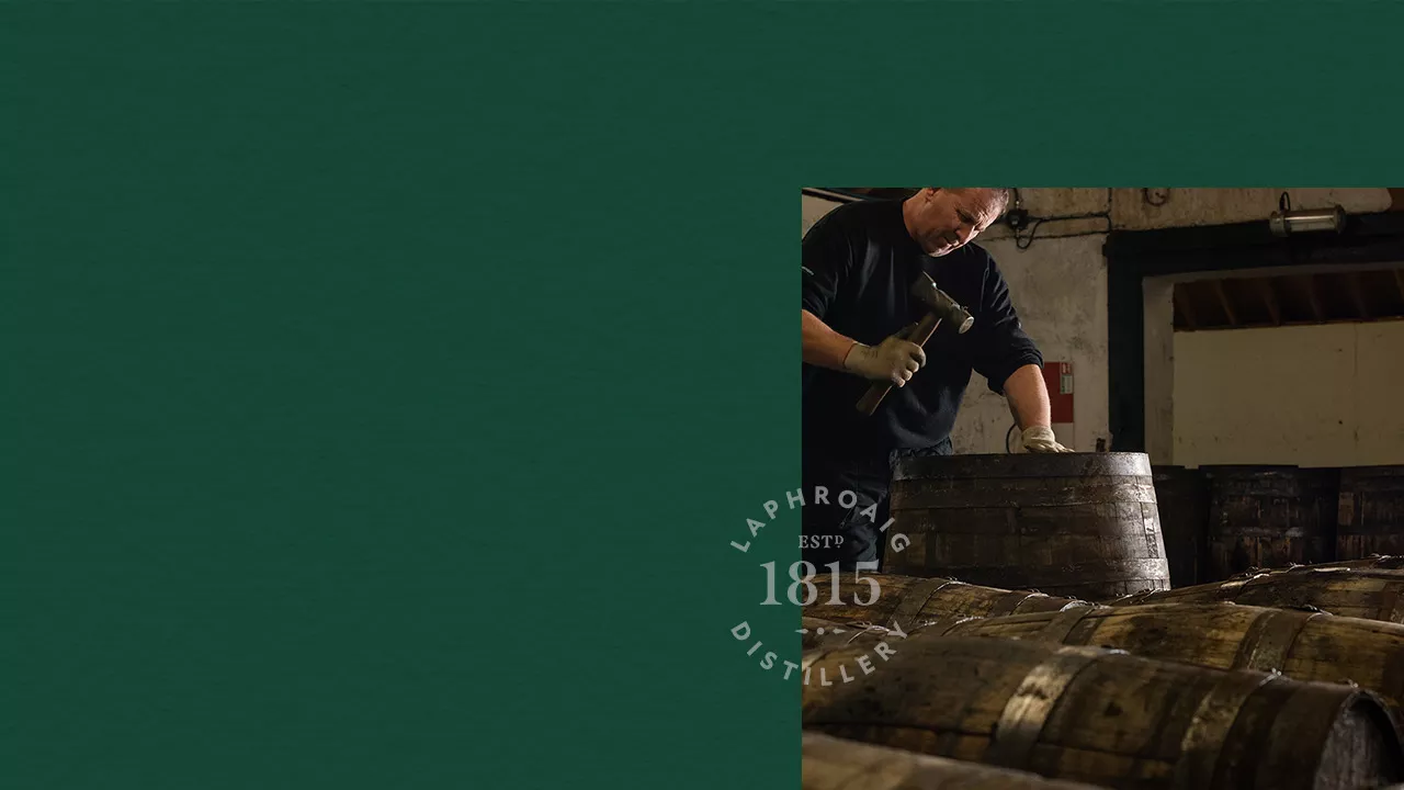 Picture of a man hammering a Laphroaig barrel on dark green background with a Laphroaig Distillery stamp on it