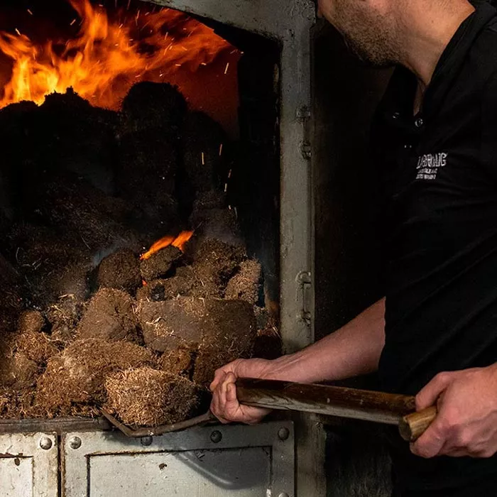 A person shoveling peat into Laphroaig kilns