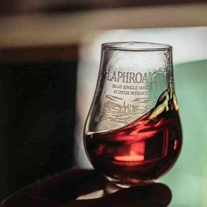 A hand in the shadows holding a dram filled pouring Cairdeas 2021