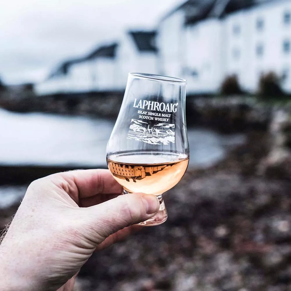 A hand holding up a dram filled with Laphroaig Cairdeas Port & Wine