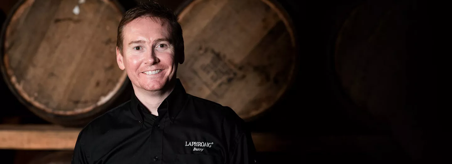 Distillery Manager Barry MacAffer smiling in front of a whisky barrel shelf