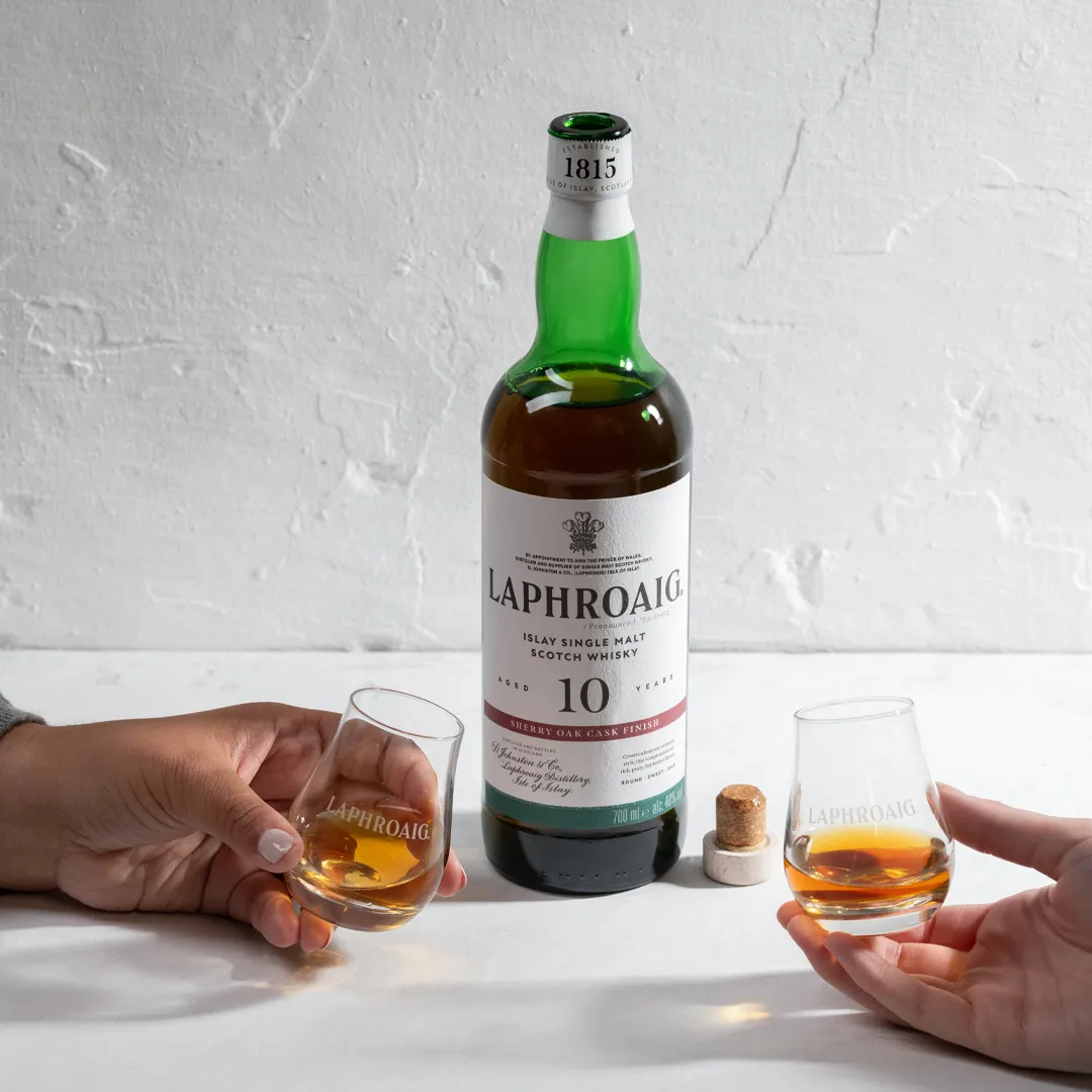 Sherry Oak Laphroaig bottle on a table with two glasses of drams in hands