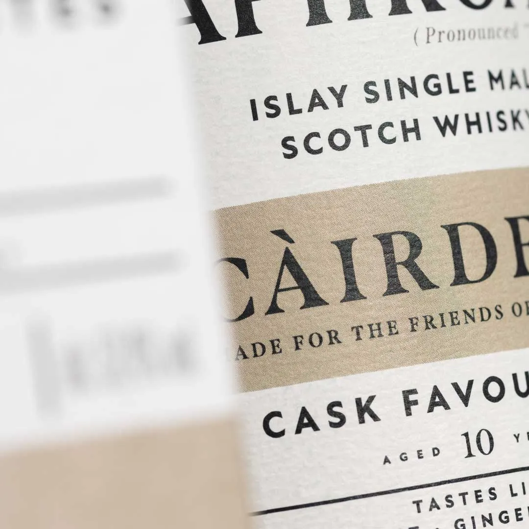Close-up detail of a Laphroaig Càirdeas whisky bottle label showing the words “Islay Single Malt Scotch Whisky” and “Càirdeas” on a cream label.