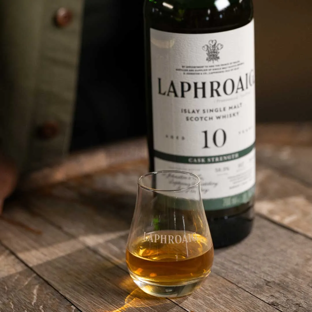 Glass of Laphroaig whisky with a bottle of Laphroaig 10 Year Old Cask Strength Islay single malt in the background.