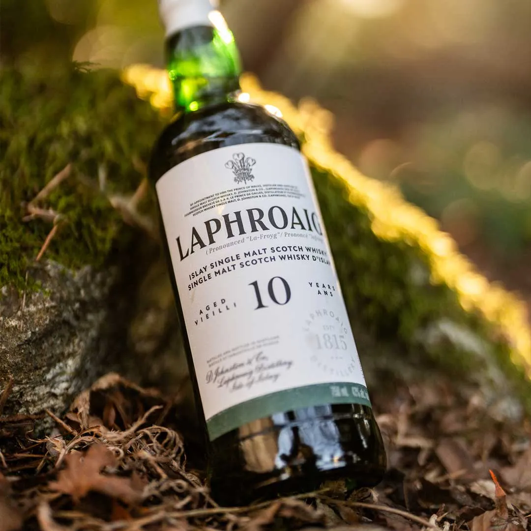 Bottle of Laphroaig 10 Year Old Islay single malt Scotch whisky resting on moss and leaves outdoors.