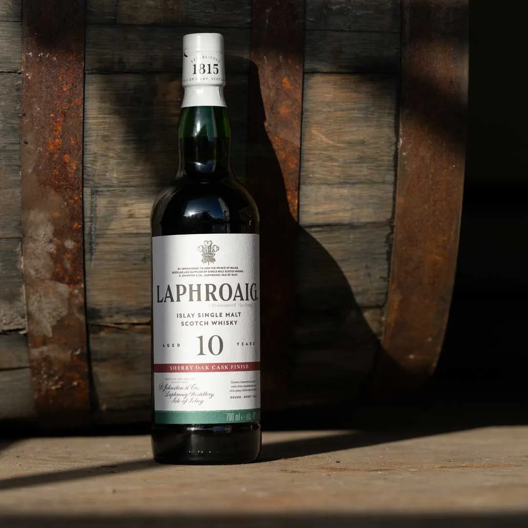 Bottle of Laphroaig 10 Year Old Sherry Oak Finish Islay single malt Scotch whisky in front of a wooden cask.
