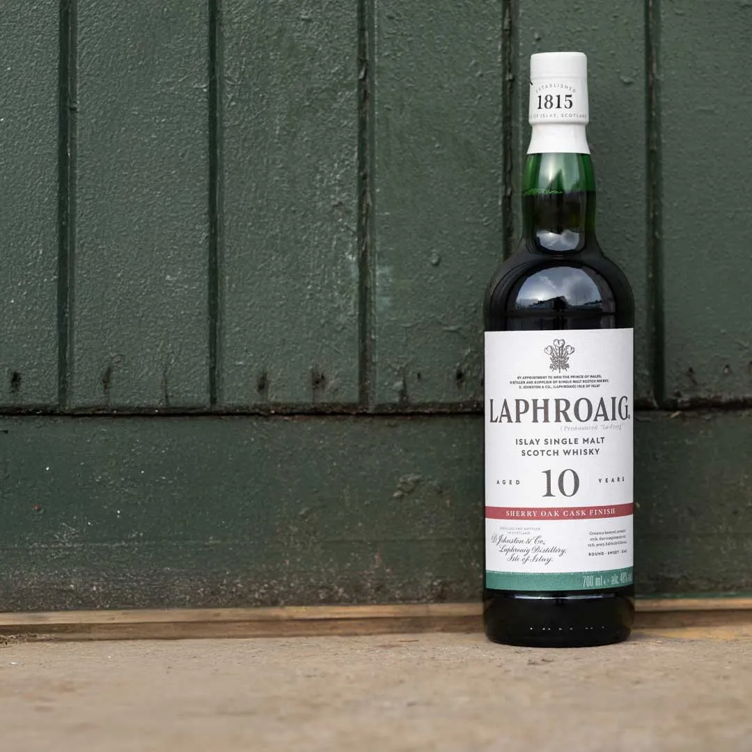Bottle of Laphroaig 10 Year Old Sherry Oak Finish Islay single malt Scotch whisky against a green wooden wall.