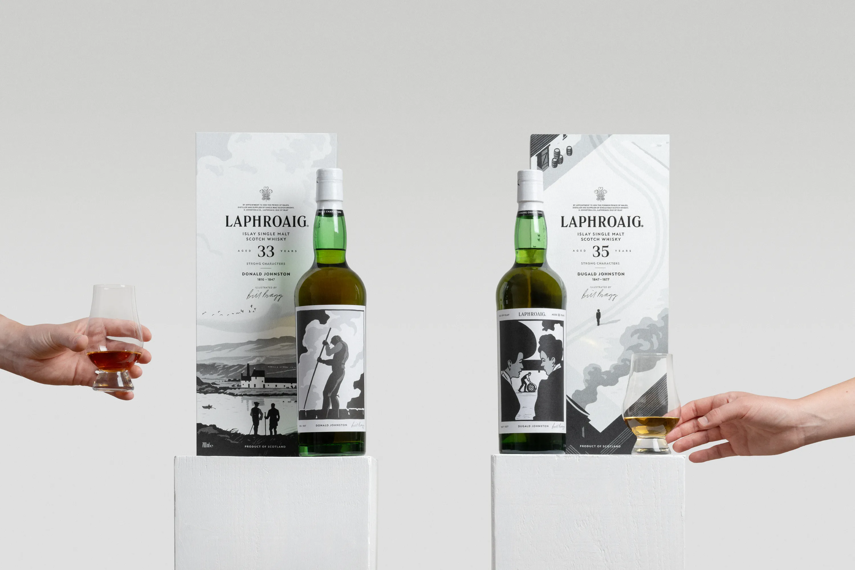 Laphroaig Strong Characters Chapter 1 33-Year-Old and Chapter 2 35-Year-Old whiskies displayed side by side with their illustrated presentation boxes, as two hands hold tasting glasses of whisky.
