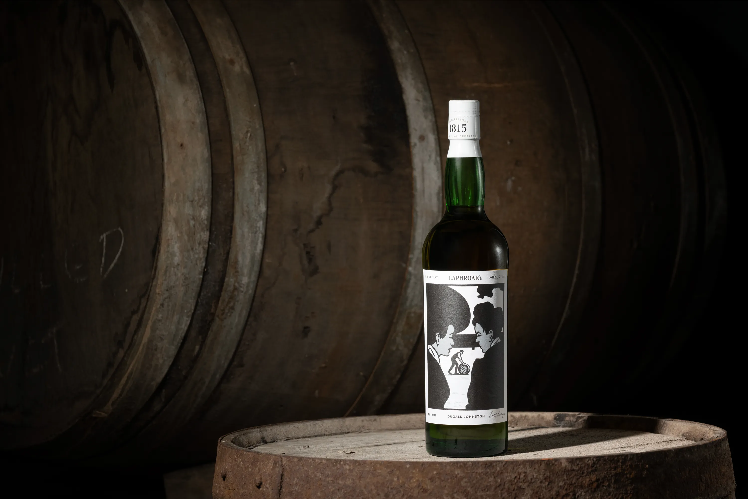 Laphroaig Strong Characters Chapter 2 35-Year-Old whisky bottle displayed on an oak cask, surrounded by ageing barrels at the distillery.