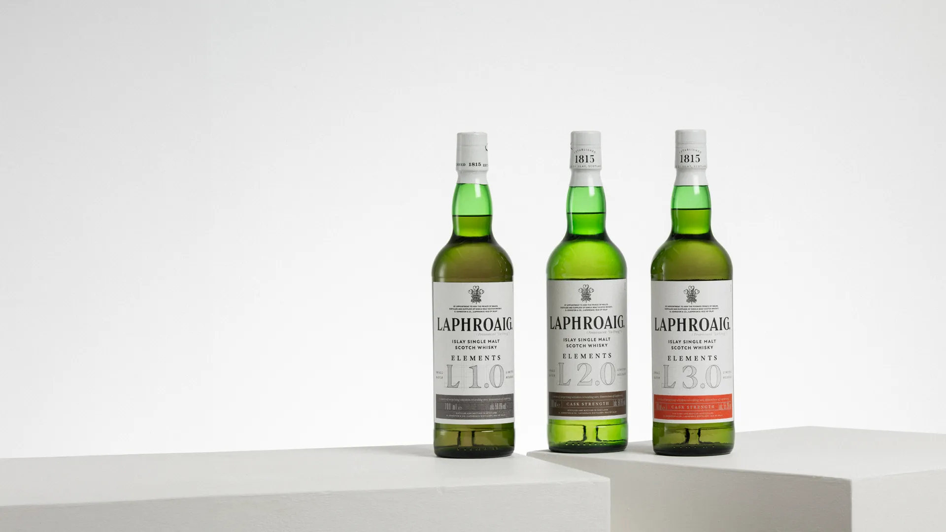 Three Laphroaig Elements Islay single malt Scotch whisky bottles displayed on white plinths.